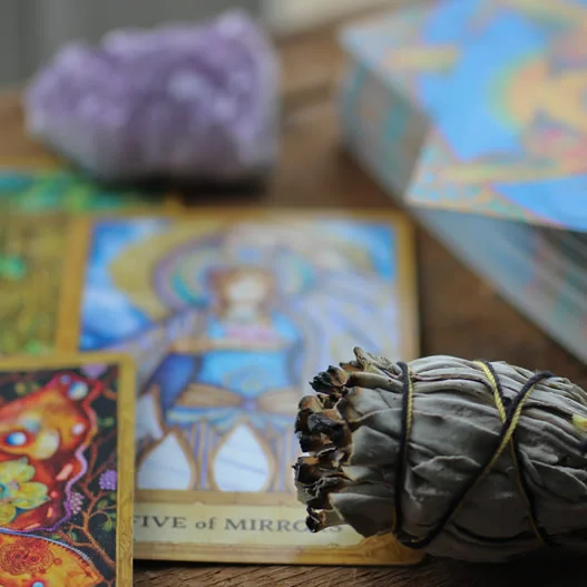 Tarot cards, sage bundle, and amethyst crystal on a wooden table